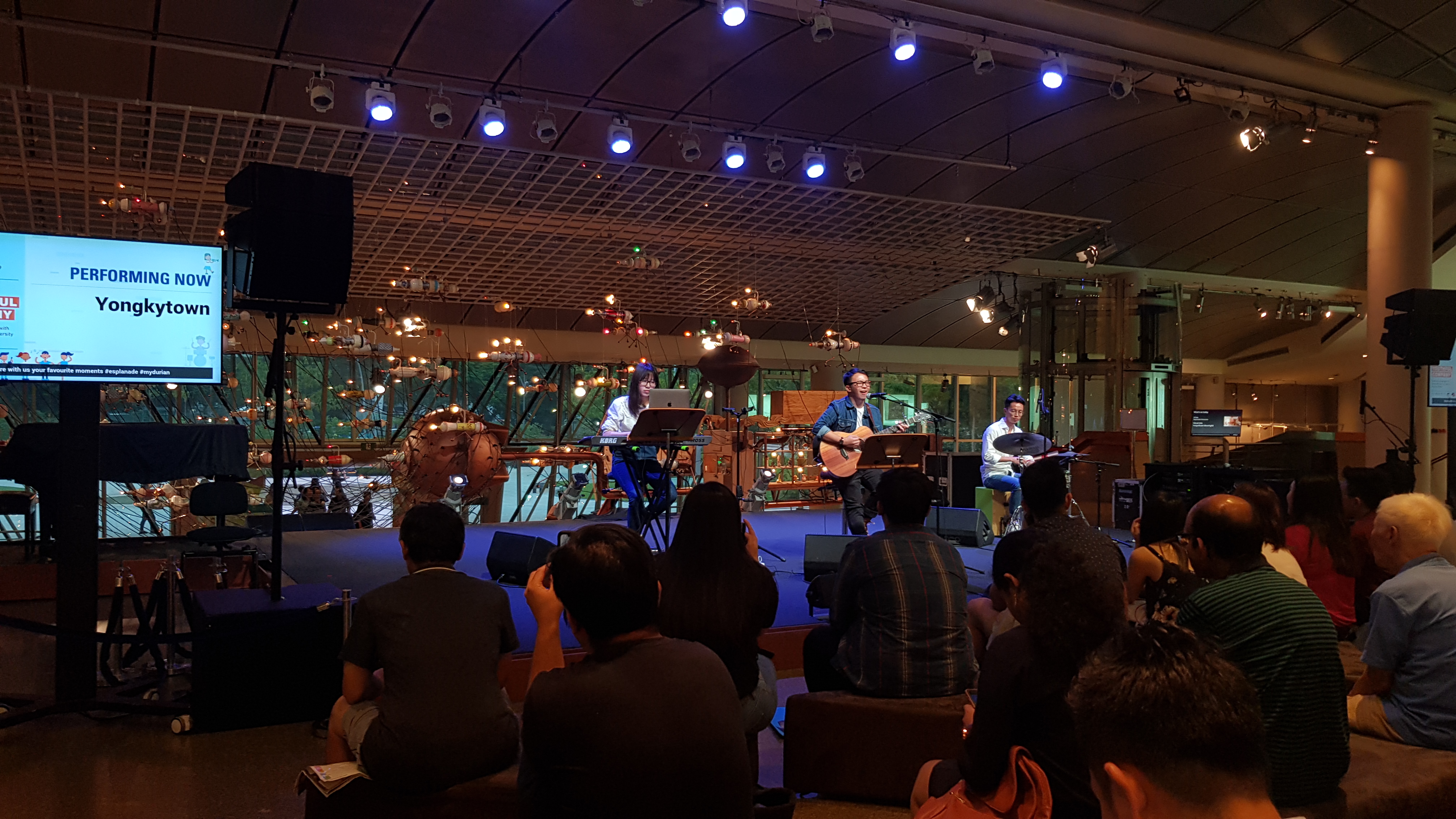 Yongkytown performing with a keyboardist and drummer in the Esplanade Concourse