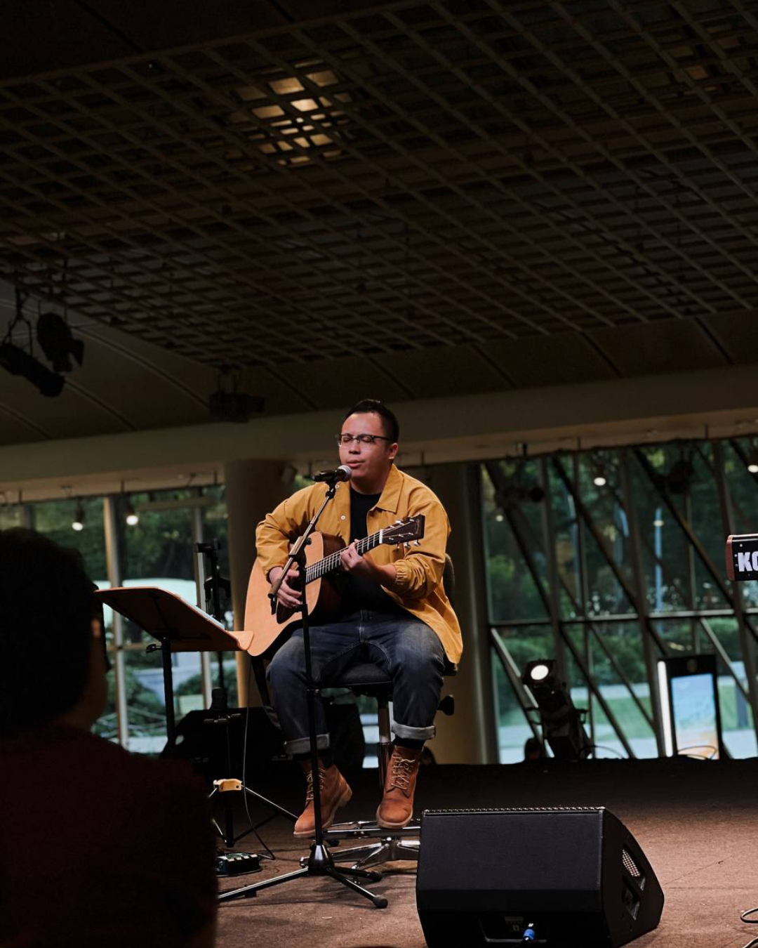 Yongkytown singing and playing guitar on stage in a mustard jacket